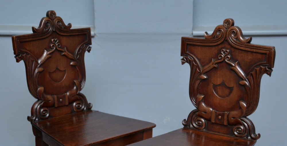 A pair of Regency mahogany hall chairs featuring carved scroll backs with shield motifs and turned reeded front legs. View II