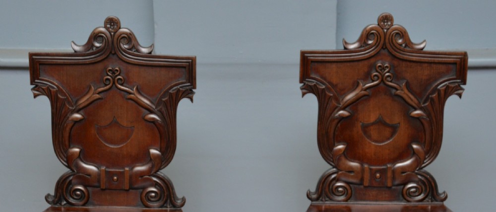 A pair of Regency mahogany hall chairs featuring carved scroll backs with shield motifs and turned reeded front legs. View IV