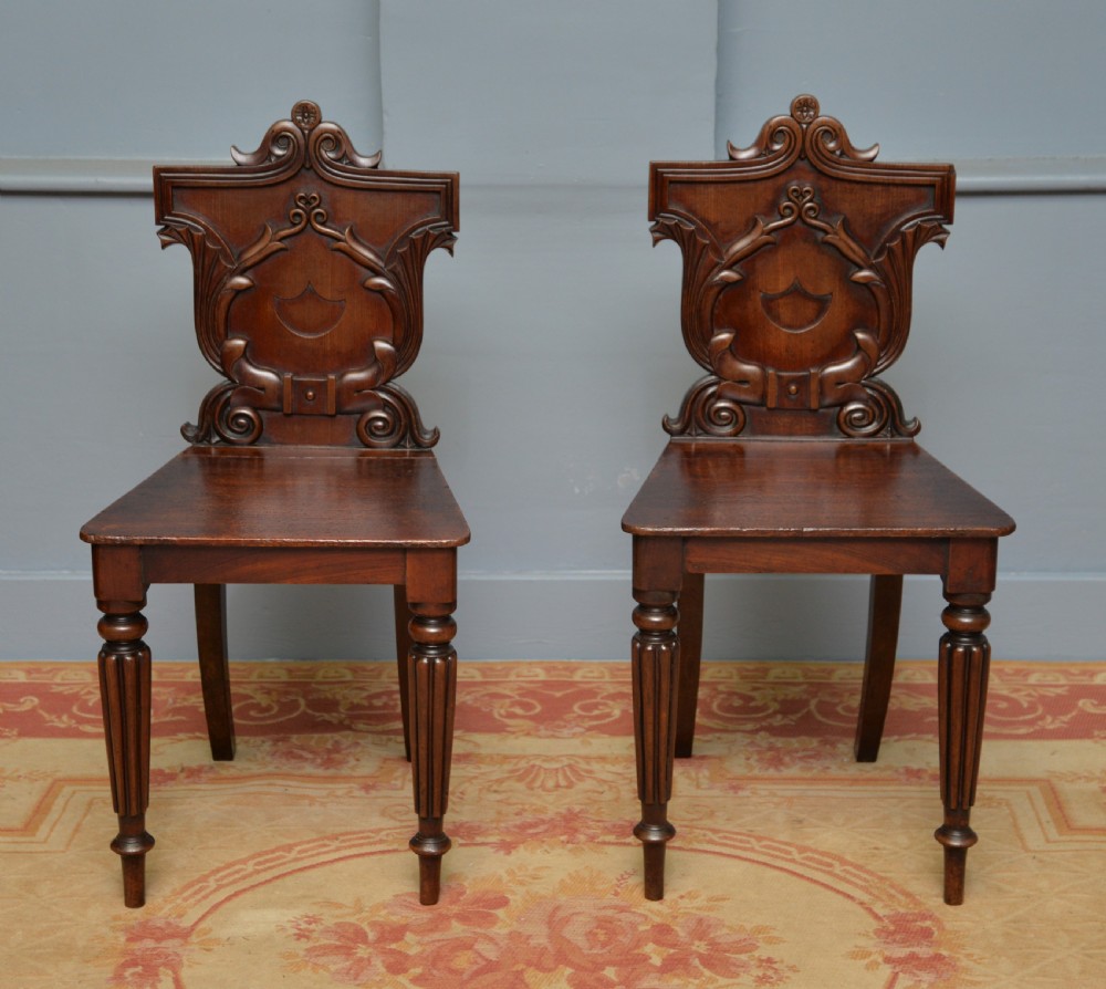 A pair of Regency mahogany hall chairs featuring carved scroll backs with shield motifs and turned reeded front legs. View V