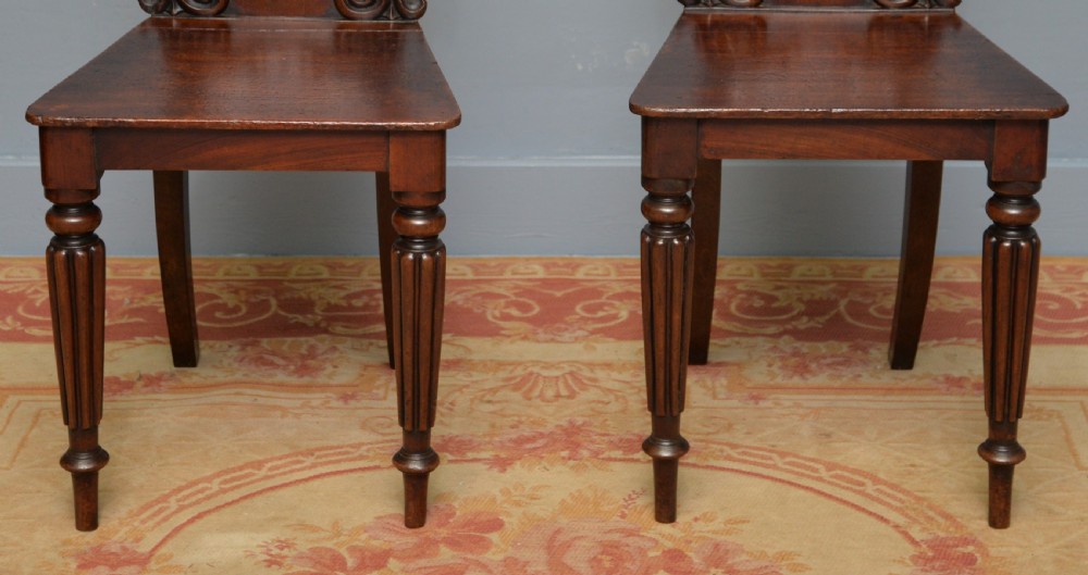 A pair of Regency mahogany hall chairs featuring carved scroll backs with shield motifs and turned reeded front legs. View VI