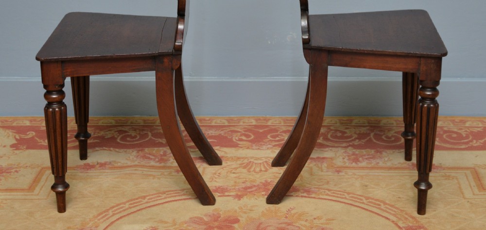 A pair of Regency mahogany hall chairs featuring carved scroll backs with shield motifs and turned reeded front legs. View VII