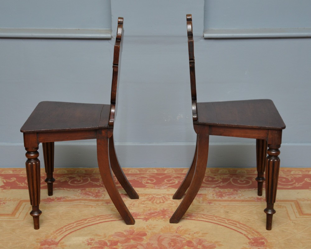 A pair of Regency mahogany hall chairs featuring carved scroll backs with shield motifs and turned reeded front legs. View VIII