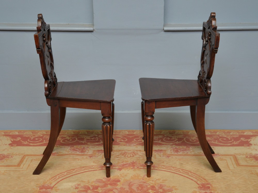 A pair of Regency mahogany hall chairs featuring carved scroll backs with shield motifs and turned reeded front legs. View IX