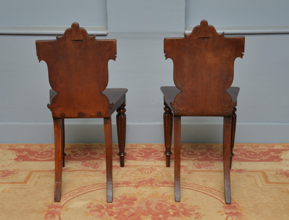 A pair of Regency mahogany hall chairs featuring carved scroll backs with shield motifs and turned reeded front legs. View XI