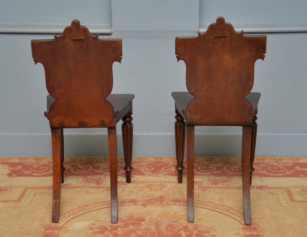 A pair of Regency mahogany hall chairs featuring carved scroll backs with shield motifs and turned reeded front legs. View XII