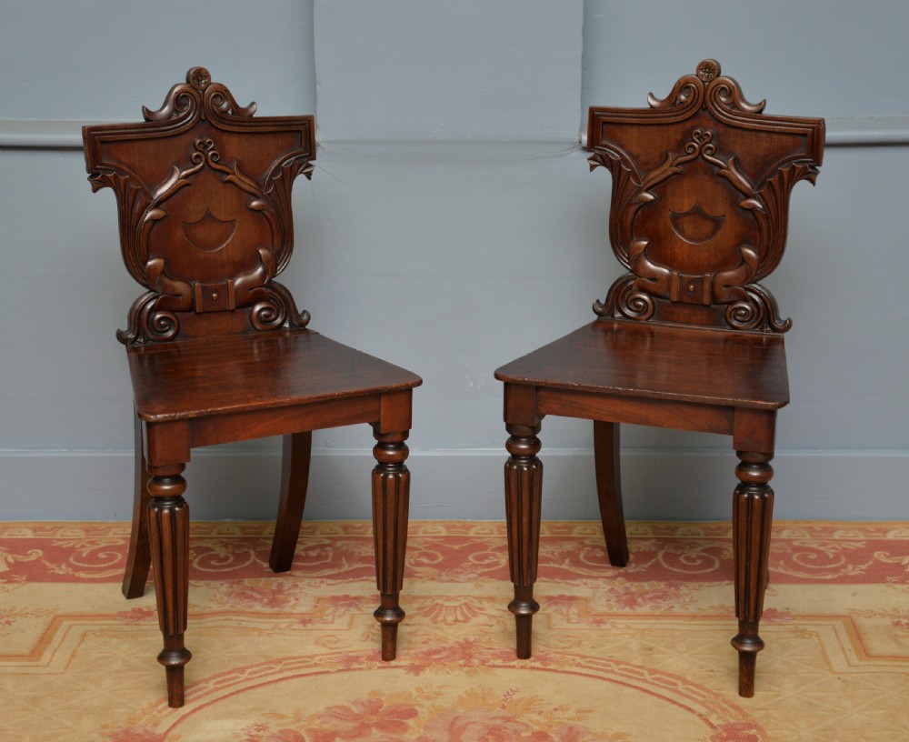 A pair of Regency mahogany hall chairs featuring carved scroll backs with shield motifs and turned reeded front legs. View XIV