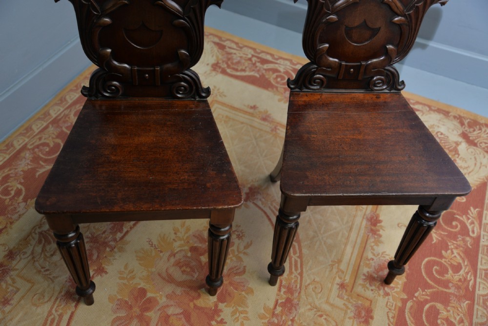 A pair of Regency mahogany hall chairs featuring carved scroll backs with shield motifs and turned reeded front legs. View XV