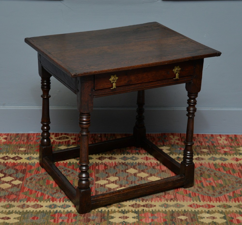 A seventeenth-century dark oak side table with turned legs, a frieze drawer with brass handles, and a low box stretcher.