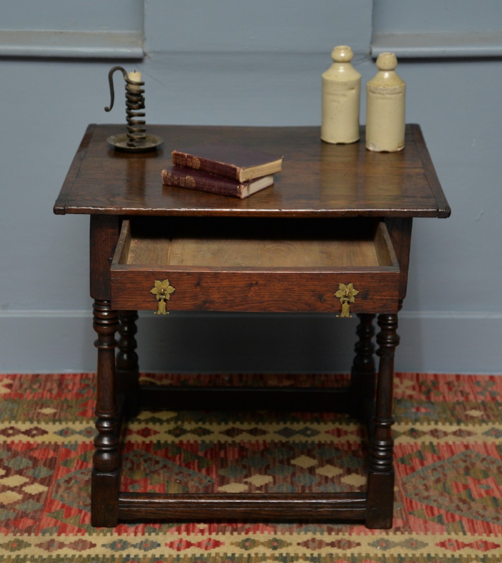 A seventeenth-century dark oak side table with turned legs, a frieze drawer with brass handles, and a low box stretcher. View V