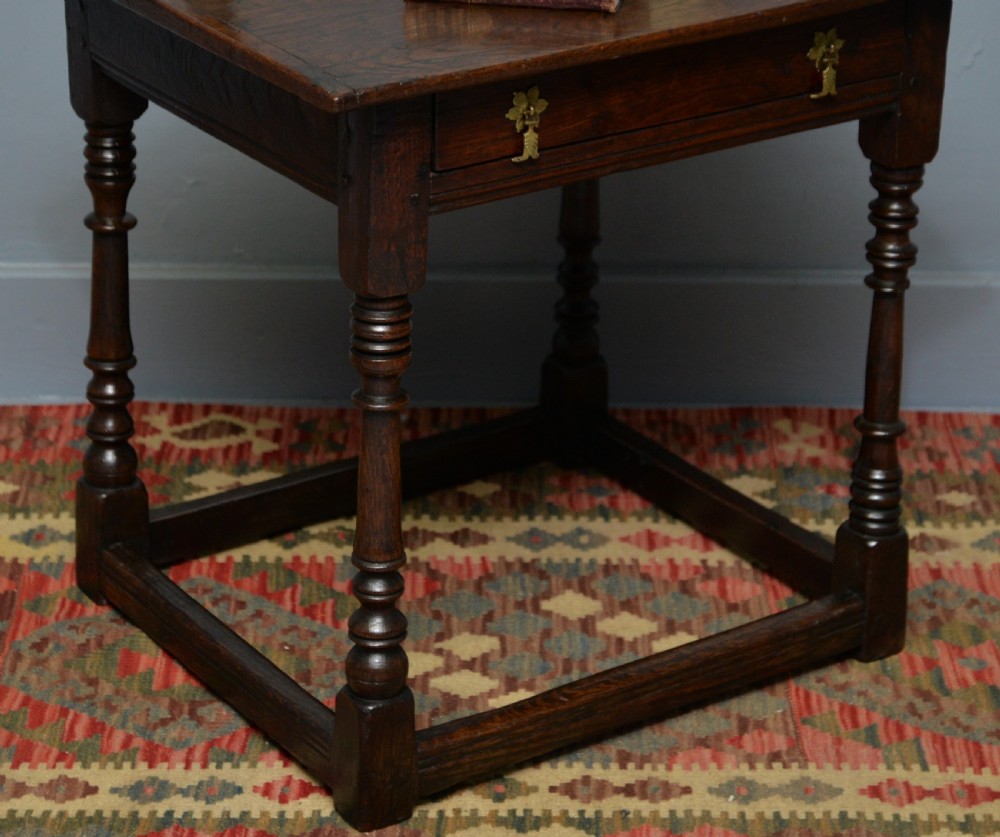 A seventeenth-century dark oak side table with turned legs, a frieze drawer with brass handles, and a low box stretcher. View VI