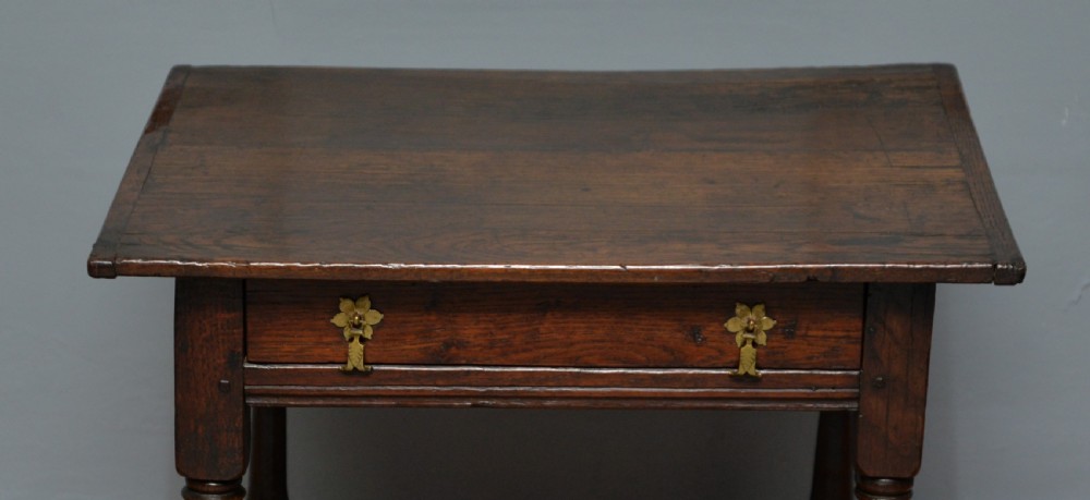 A seventeenth-century dark oak side table with turned legs, a frieze drawer with brass handles, and a low box stretcher. View VII