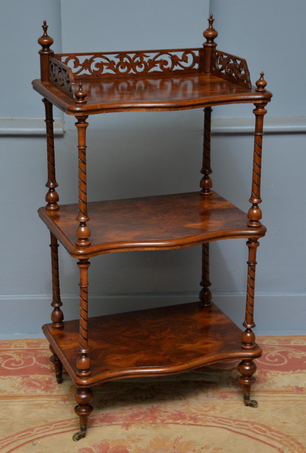 A three-tier Victorian burr walnut whatnot featuring barley twist columns, a pierced fretwork top gallery, shaped shelves, and brass castors. View IX