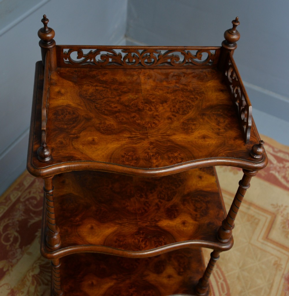 A three-tier Victorian burr walnut whatnot featuring barley twist columns, a pierced fretwork top gallery, shaped shelves, and brass castors. View XV