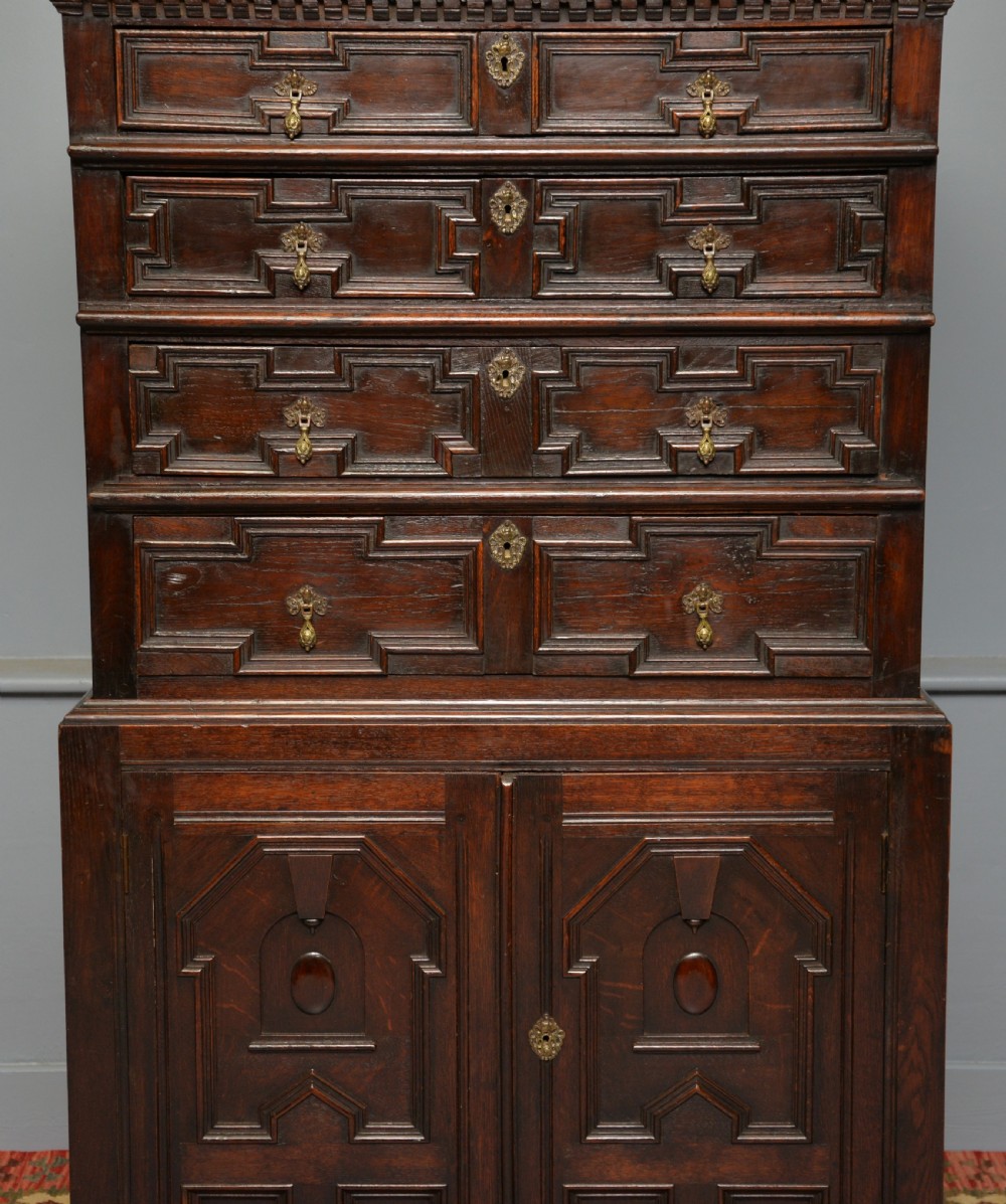 A tall dark oak Charles II chest featuring geometric moulded drawers and brass tear-drop handles above a two-door cupboard. View III