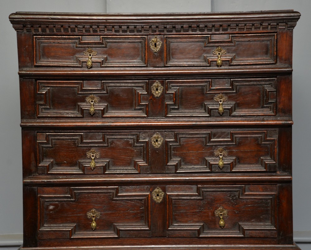 A tall dark oak Charles II chest featuring geometric moulded drawers and brass tear-drop handles above a two-door cupboard. View IV