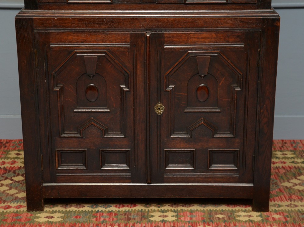 A tall dark oak Charles II chest featuring geometric moulded drawers and brass tear-drop handles above a two-door cupboard. View V