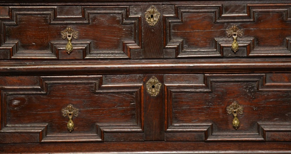A tall dark oak Charles II chest featuring geometric moulded drawers and brass tear-drop handles above a two-door cupboard. View VII