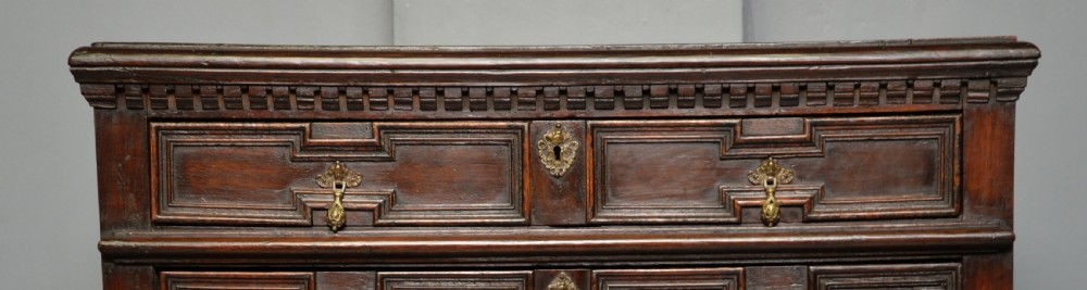 A tall dark oak Charles II chest featuring geometric moulded drawers and brass tear-drop handles above a two-door cupboard. View VIII