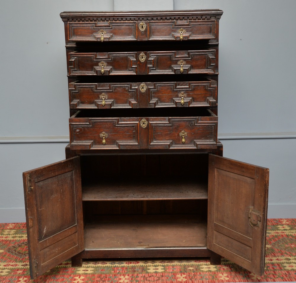 A tall dark oak Charles II chest featuring geometric moulded drawers and brass tear-drop handles above a two-door cupboard. View X