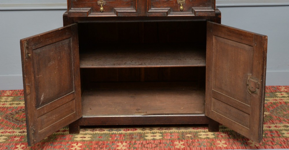 A tall dark oak Charles II chest featuring geometric moulded drawers and brass tear-drop handles above a two-door cupboard. View XI