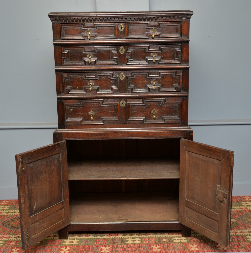 A tall dark oak Charles II chest featuring geometric moulded drawers and brass tear-drop handles above a two-door cupboard. View XII