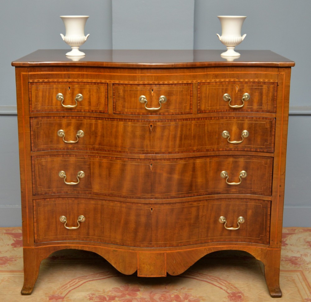 A George III mahogany chest of drawers featuring a serpentine front face, inlaid stringing borders, and brass swan-neck handles.