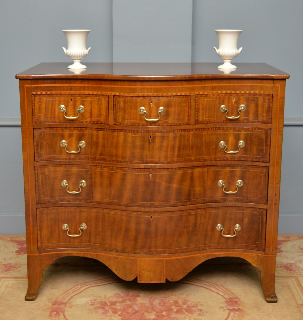 A George III mahogany chest of drawers featuring a serpentine front face, inlaid stringing borders, and brass swan-neck handles. View II