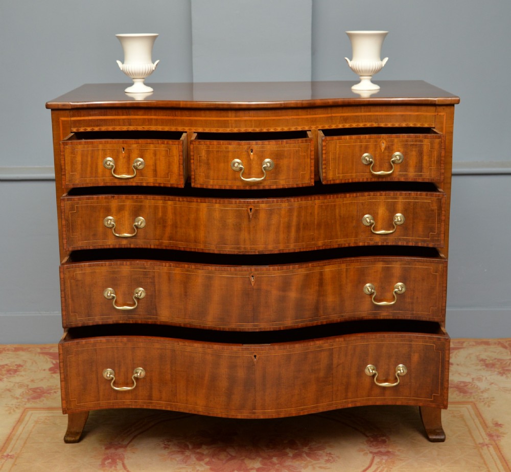 A George III mahogany chest of drawers featuring a serpentine front face, inlaid stringing borders, and brass swan-neck handles. View IV