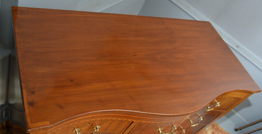 A George III mahogany chest of drawers featuring a serpentine front face, inlaid stringing borders, and brass swan-neck handles. View V