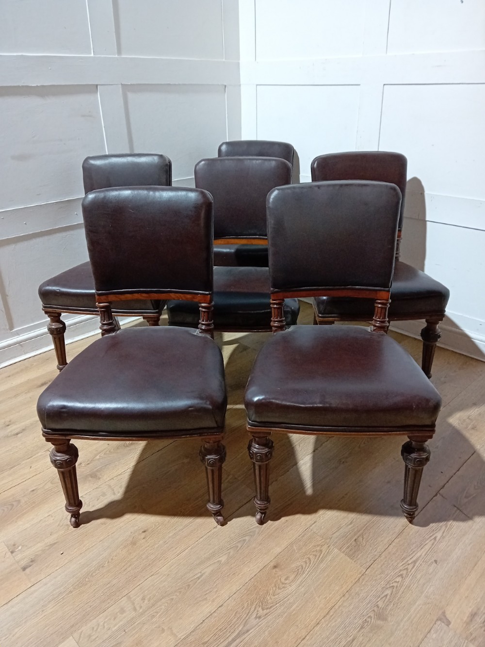 A set of six Victorian Gothic Reform side chairs featuring dark brown leather upholstery and turned wooden front legs on brass castors.