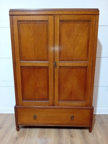 An Edwardian oak compactum wardrobe featuring two panelled doors with chevron oak veneers above a wide single drawer with brass drop handles.