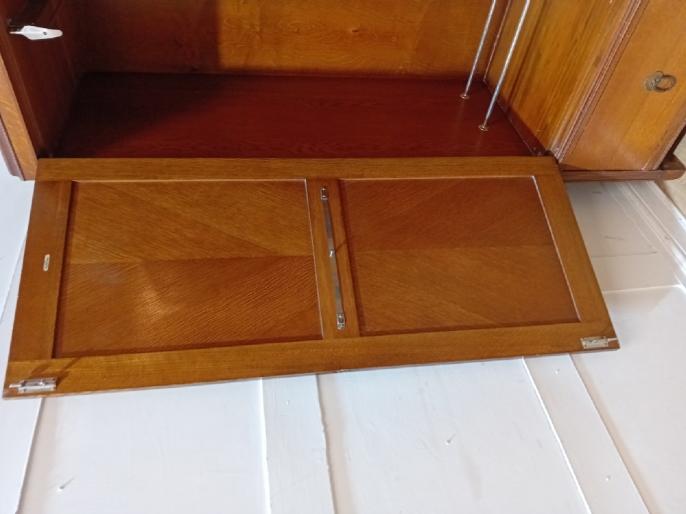 An Edwardian oak compactum wardrobe featuring two panelled doors with chevron oak veneers above a wide single drawer with brass drop handles. View IV