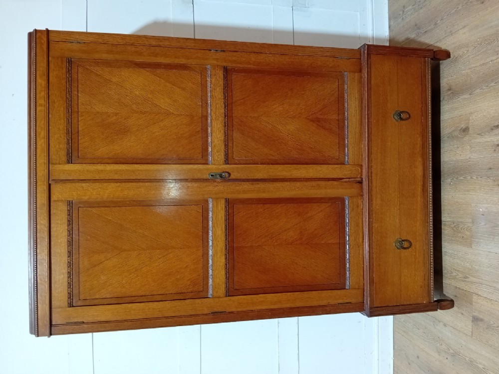 An Edwardian oak compactum wardrobe featuring two panelled doors with chevron oak veneers above a wide single drawer with brass drop handles. View X
