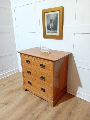 A late nineteenth-century satinwood chest of drawers with three full-width drawers and dark metal drop handles. View II