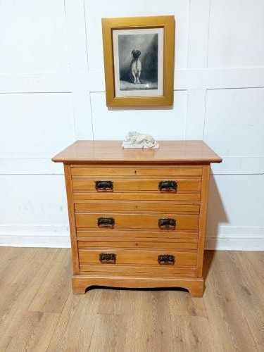 A late nineteenth-century satinwood chest of drawers with three full-width drawers and dark metal drop handles. View IV