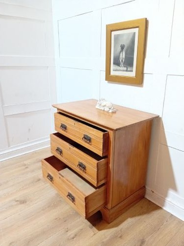 A late nineteenth-century satinwood chest of drawers with three full-width drawers and dark metal drop handles. View VII