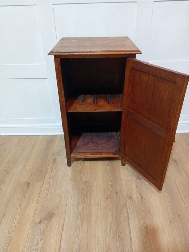 A warm brown Arts and Crafts oak hall cupboard with a two-panel door and a moulded flat top. View V