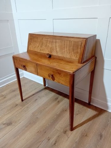 An Arts and Crafts Cotswold School wooden writing bureau featuring a fall-front upper section, two lower drawers with turned wooden knobs, and slender tapered legs. View II