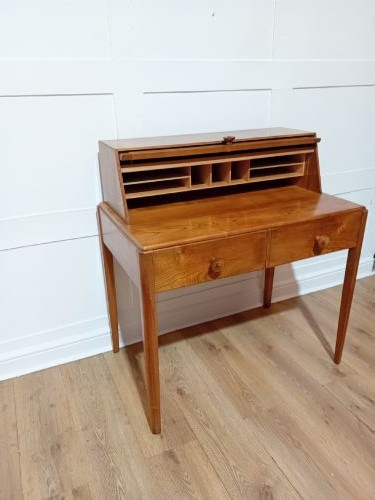 An Arts and Crafts Cotswold School wooden writing bureau featuring a fall-front upper section, two lower drawers with turned wooden knobs, and slender tapered legs. View VII