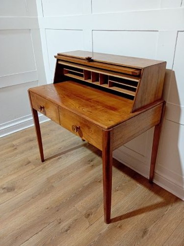 An Arts and Crafts Cotswold School wooden writing bureau featuring a fall-front upper section, two lower drawers with turned wooden knobs, and slender tapered legs. View XIII