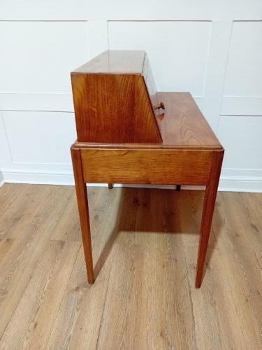 An Arts and Crafts Cotswold School wooden writing bureau featuring a fall-front upper section, two lower drawers with turned wooden knobs, and slender tapered legs. View XII