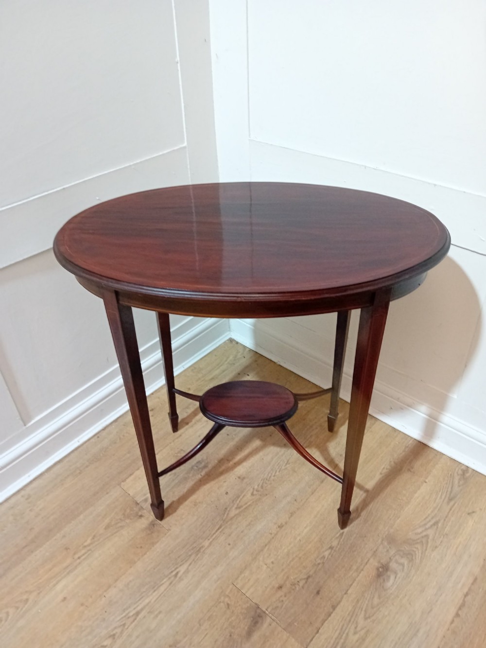 An antique oval dark mahogany occasional table featuring slender tapered legs connected by curved stretchers with a small central circular shelf.