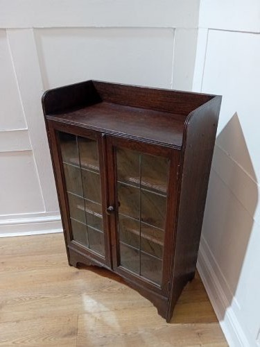 A dark oak Arts and Crafts dwarf glazed cabinet featuring twin leaded glass doors and a gallery top upstand. View VII