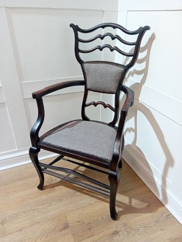 An antique dark mahogany Edwardian armchair featuring a contoured ladder back rest, padded central panel, curved armrests, and grey upholstered seat. View II