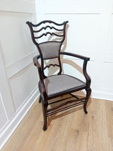 An antique dark mahogany Edwardian armchair featuring a contoured ladder back rest, padded central panel, curved armrests, and grey upholstered seat. View III