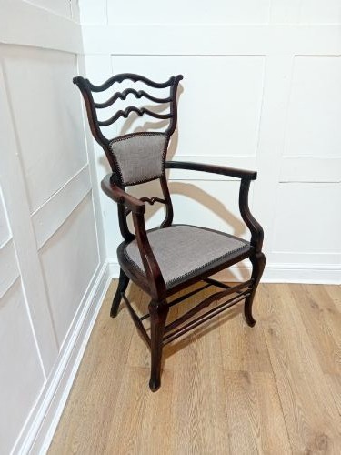 An antique dark mahogany Edwardian armchair featuring a contoured ladder back rest, padded central panel, curved armrests, and grey upholstered seat. View IV