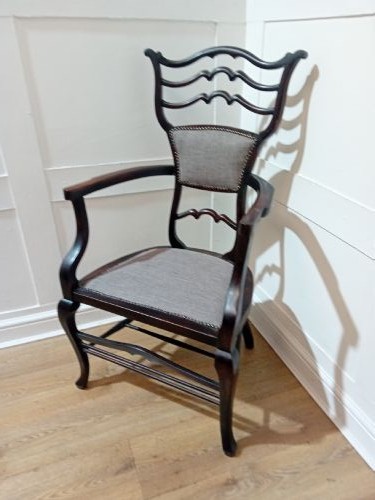 An antique dark mahogany Edwardian armchair featuring a contoured ladder back rest, padded central panel, curved armrests, and grey upholstered seat. View V