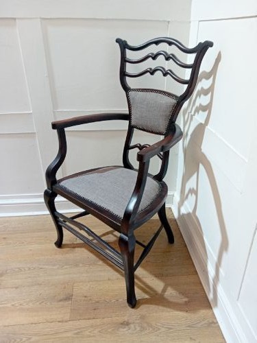 An antique dark mahogany Edwardian armchair featuring a contoured ladder back rest, padded central panel, curved armrests, and grey upholstered seat. View VI