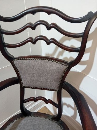 An antique dark mahogany Edwardian armchair featuring a contoured ladder back rest, padded central panel, curved armrests, and grey upholstered seat. View XII