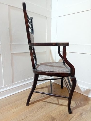 An antique dark mahogany Edwardian armchair featuring a contoured ladder back rest, padded central panel, curved armrests, and grey upholstered seat. View X